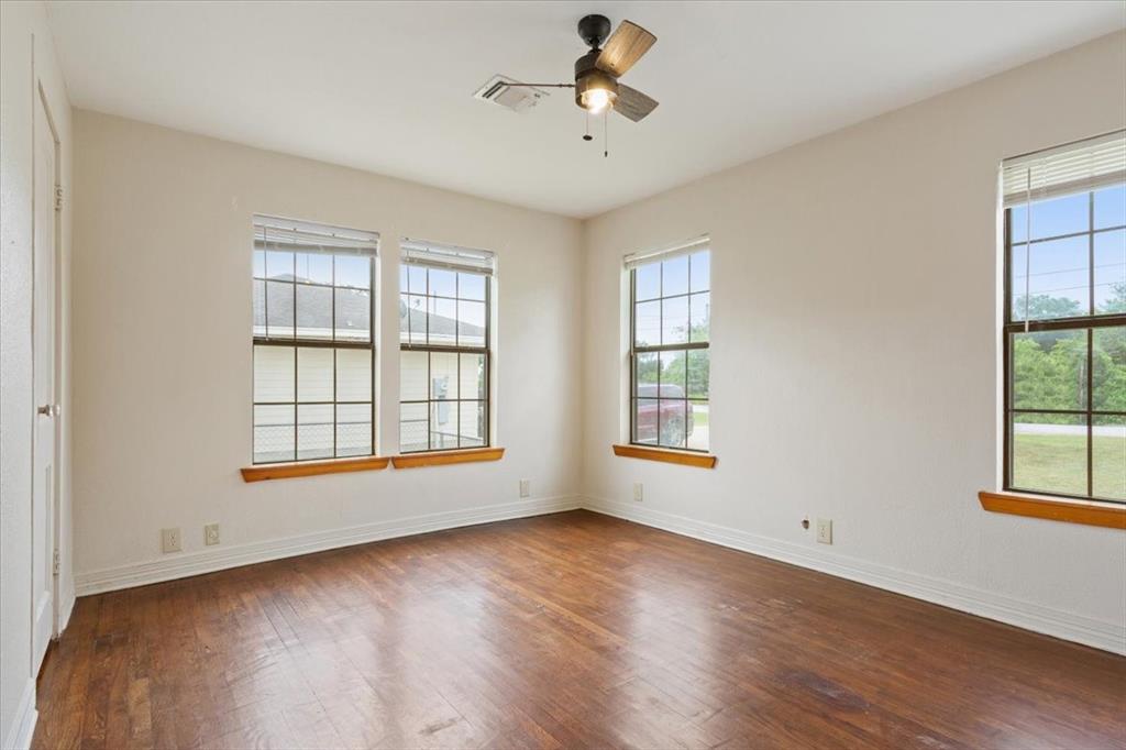 608 9th Street Hico, TX 76457 - Photo 11 of 23 Spacious room featuring rich wood-finish flooring, multiple paneled windows, white walls, and a ceiling fan with integrated lighting