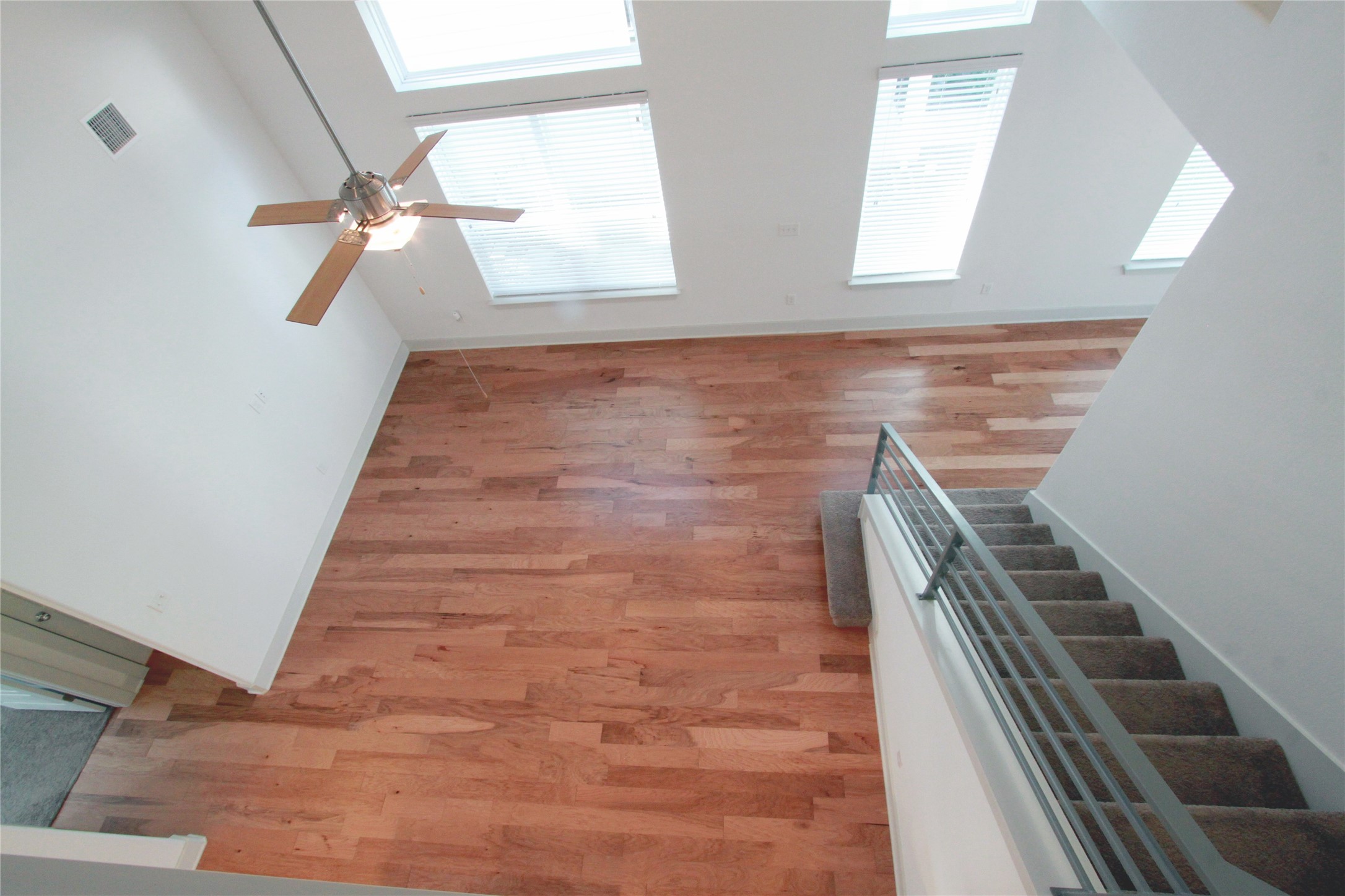 1507 Homespun Road Austin, TX 78745 - Photo 25 of 35 Expansive high-ceiling space featuring multiple skylights, wood-finish flooring, a contemporary ceiling fan, and a staircase with carpeted treads and metal railings