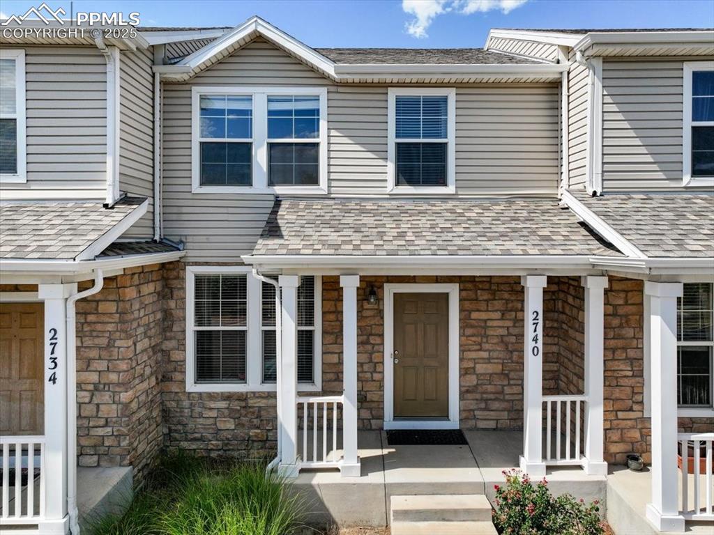 View of front of home featuring stone siding, a porch, and roof with shingles