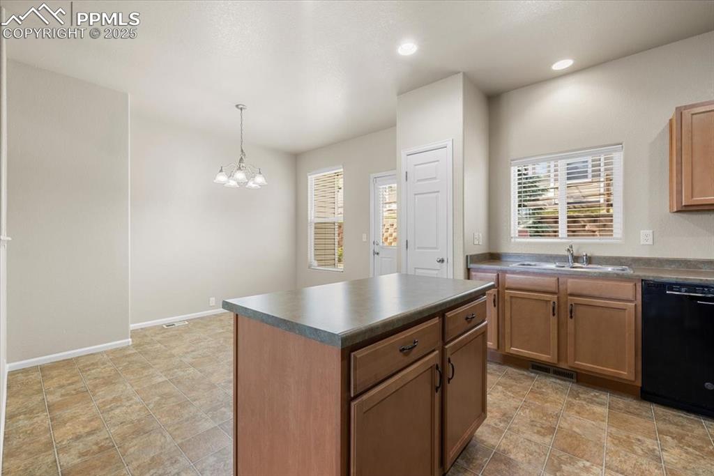 2740 Stonecrop Ridge Grove Colorado Springs, CO 80910 - Photo 16 of 42 Kitchen featuring dark countertops, dishwasher, decorative light fixtures, a chandelier, and a kitchen island