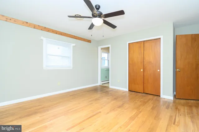 a view of an empty room with wooden floor and a ceiling fan