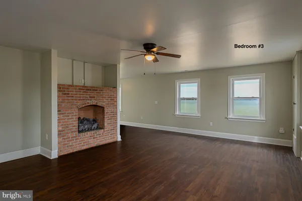 an empty room with wooden floor a fireplace and windows