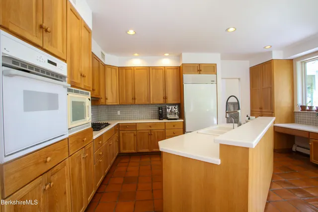 a large kitchen with stainless steel appliances a sink dishwasher a stove top oven a refrigerator with wooden cabinets and floor