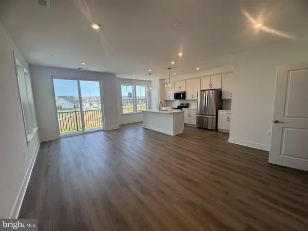 a living room with stainless steel appliances wooden floors and kitchen view