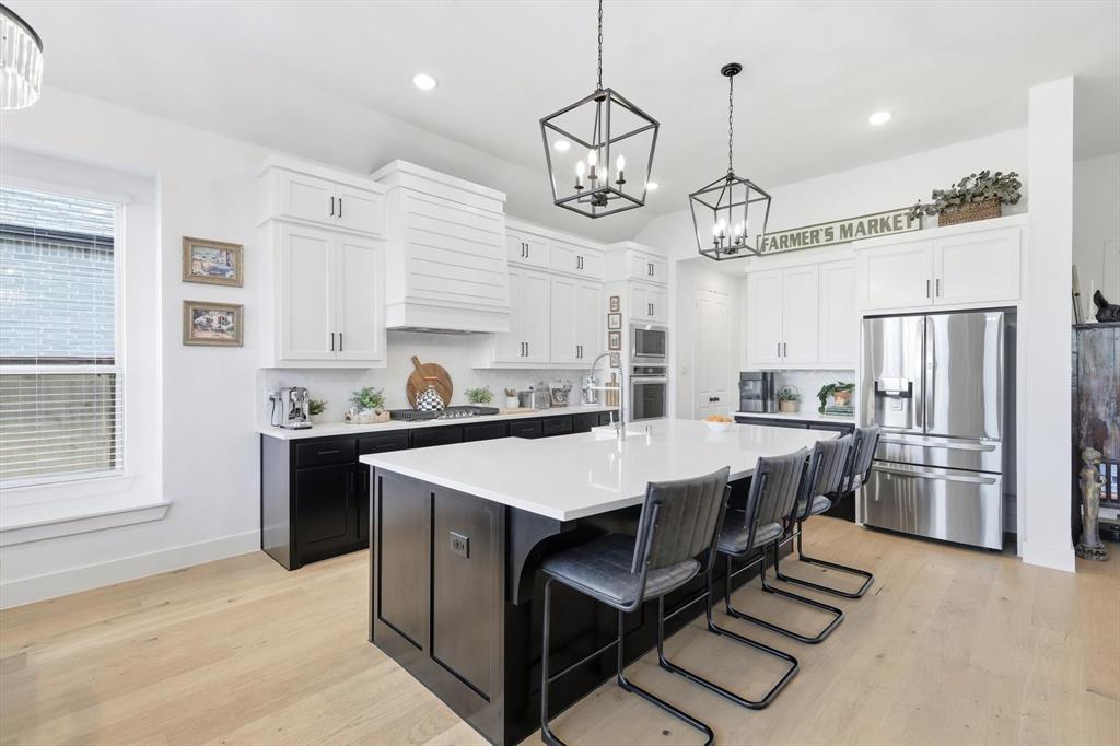 4608 Mount Vista Road Oak Point, TX 75068 - Photo 18 of 39 Open-concept kitchen featuring an expansive center island with seating, stainless steel appliances, a white tile backsplash, and light wood-finish flooring