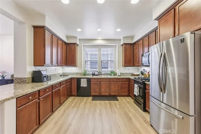 a kitchen with stainless steel appliances granite countertop a refrigerator stove a sink dishwasher and wooden cabinets with wooden floor