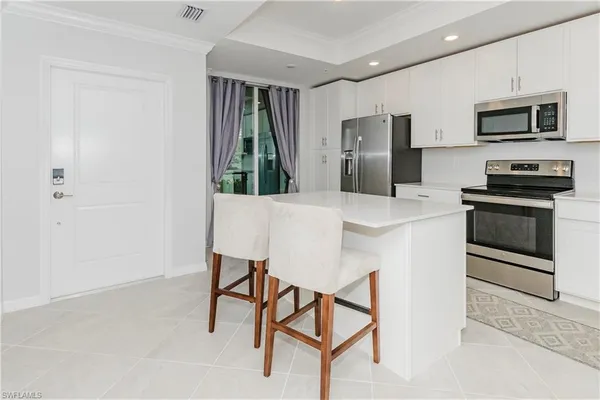 a kitchen with stainless steel appliances kitchen island granite countertop a refrigerator a stove a microwave oven with white cabinets and wooden floor