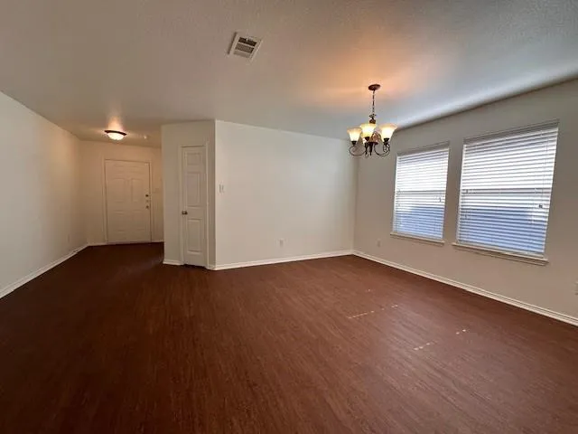 an empty room with wooden floor chandelier and windows