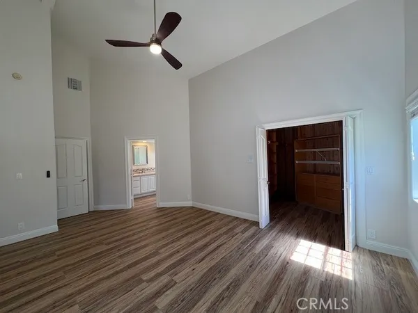 a view of an empty room with wooden floor ceiling fan