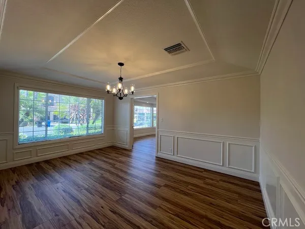 an empty room with wooden floor chandelier and windows