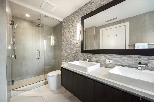 a bathroom with a double vanity sink mirror double shower and a toilet