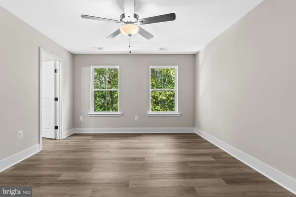 an empty room with wooden floor chandelier fan and windows