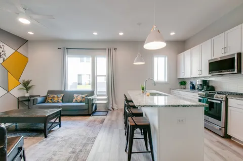 a kitchen with stainless steel appliances kitchen island granite countertop a dining table chairs and a refrigerator