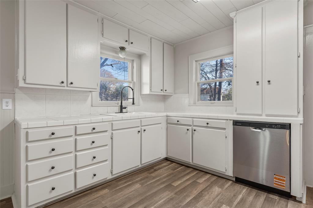 2912 Edmond Avenue Waco, TX 76707 - Photo 10 of 30 Kitchen featuring tile countertops, stainless steel dishwasher, dark wood-style flooring, white cabinetry, and ornamental molding