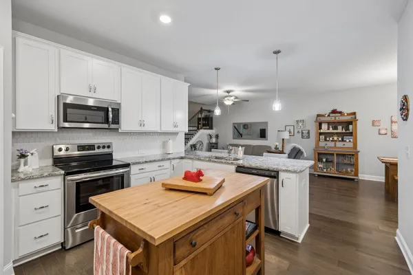 a open kitchen with stainless steel appliances a stove top oven a sink dishwasher and white cabinets with wooden floor