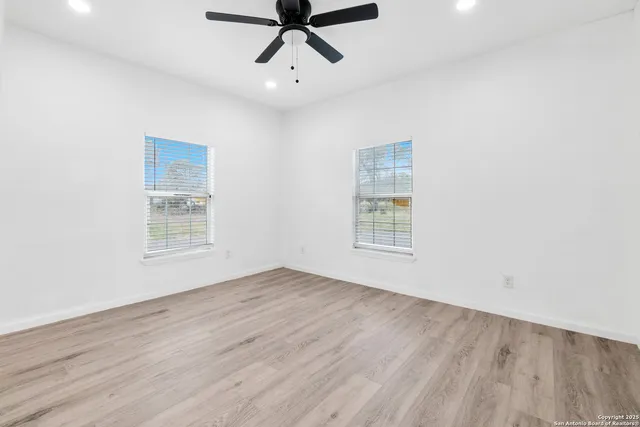 an empty room with wooden floor a ceiling fan and windows