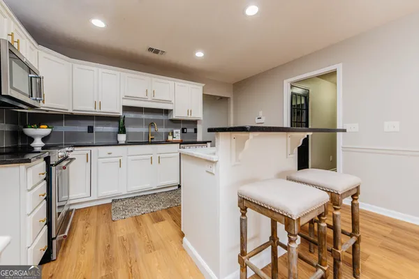 a kitchen with stainless steel appliances granite countertop a refrigerator a stove top oven and a sink with wooden floor