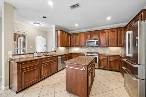 a kitchen with stainless steel appliances granite countertop wooden cabinets a sink a stove a refrigerator and island