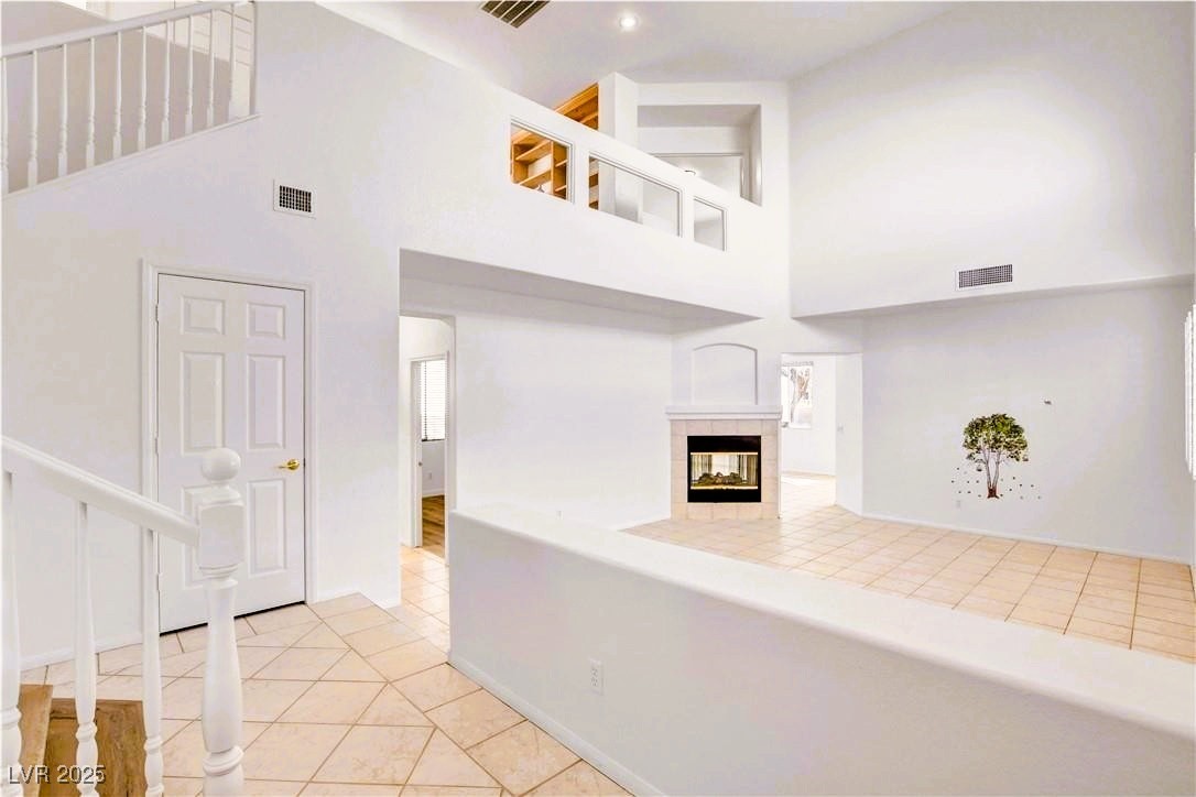10247 Splendor Ridge Avenue Las Vegas, NV 89135 - Photo 1 of 38 Unfurnished living room with light tile patterned flooring, a fireplace, a towering ceiling, and stairway