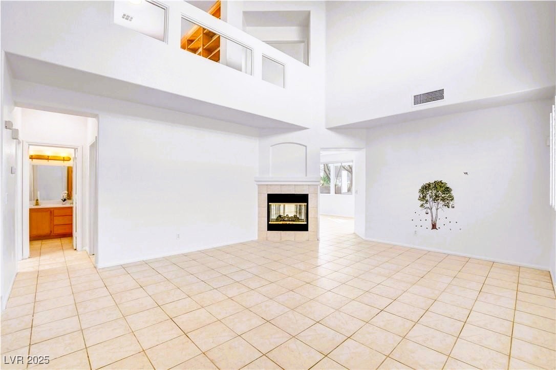 10247 Splendor Ridge Avenue Las Vegas, NV 89135 - Photo 25 of 38 Unfurnished living room with a tiled fireplace, a towering ceiling, and light tile patterned flooring