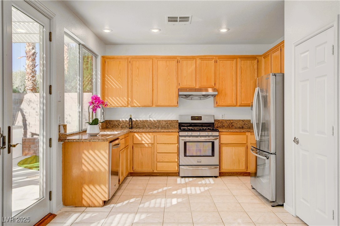 10247 Splendor Ridge Avenue Las Vegas, NV 89135 - Photo 28 of 38 Kitchen featuring appliances with stainless steel finishes, dark stone countertops, light tile patterned floors, recessed lighting, and under cabinet range hood