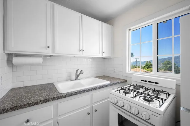 a kitchen with sink a stove and white cabinets with wooden floor