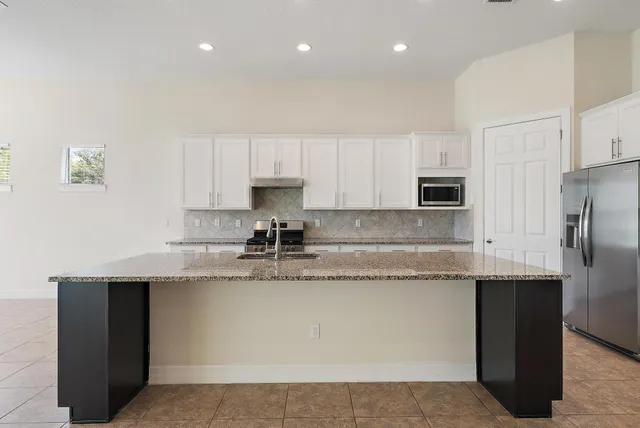 a kitchen with stainless steel appliances granite countertop a sink a stove a refrigerator and white cabinets