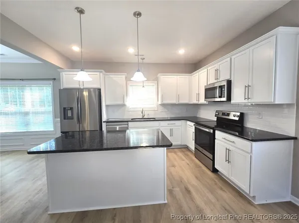 a large kitchen with granite countertop a stove a sink a refrigerator and a microwave