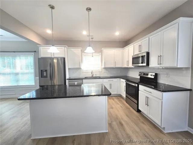 a large kitchen with granite countertop a stove a sink a refrigerator and a microwave