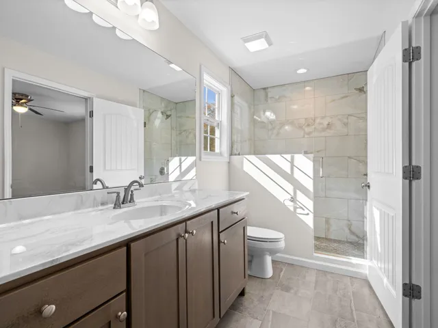 a bathroom with a granite countertop sink a toilet a mirror and shower