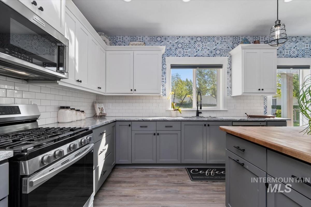 15015 Leon Lane Caldwell, ID 83607 - Photo 6 of 44 Modern kitchen featuring two-tone cabinetry with white upper cabinets and gray lower cabinets, a stainless steel range with overhead microwave, a white subway tile backsplash, and wood-finish flooring