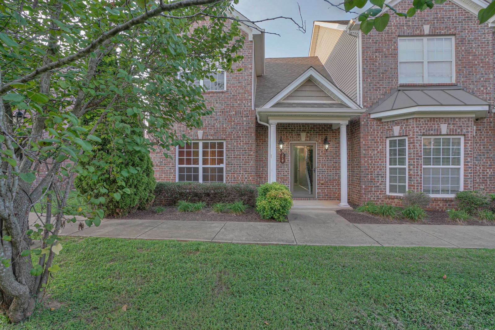 a view of a brick house with a yard and large trees