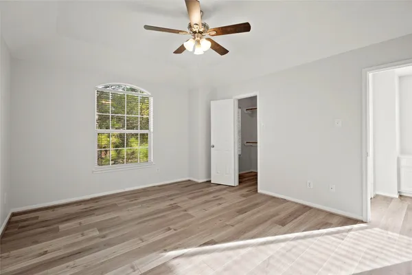 an empty room with wooden floor chandelier fan and windows
