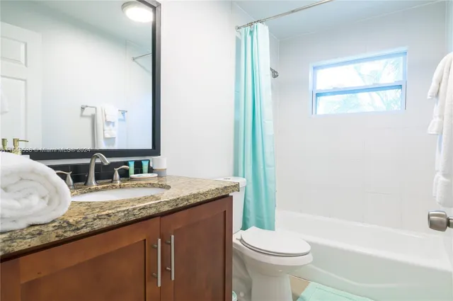 a bathroom with a granite countertop sink toilet mirror and bathtub