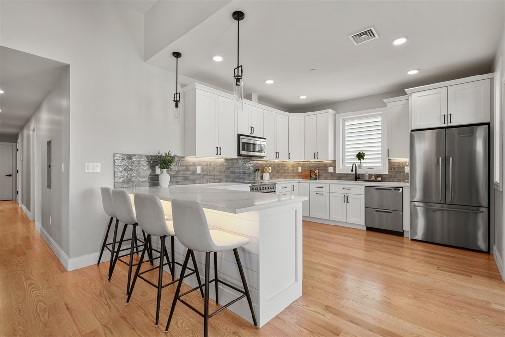60 Fuller Street, Unit PH5 Boston, MA 02124 - Photo 6 of 32 a kitchen with stainless steel appliances granite countertop a refrigerator a stove top oven a sink dishwasher a dining table and chairs with wooden floor