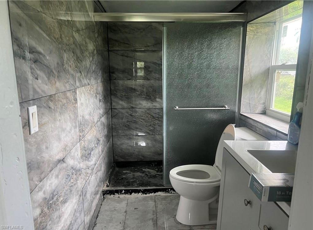 160 Brooks Road North Fort Myers, FL 33917 - Photo 10 of 19 Bathroom featuring full-height stone-look tile, a sliding glass shower enclosure, and a vanity with a white countertop and integrated sink