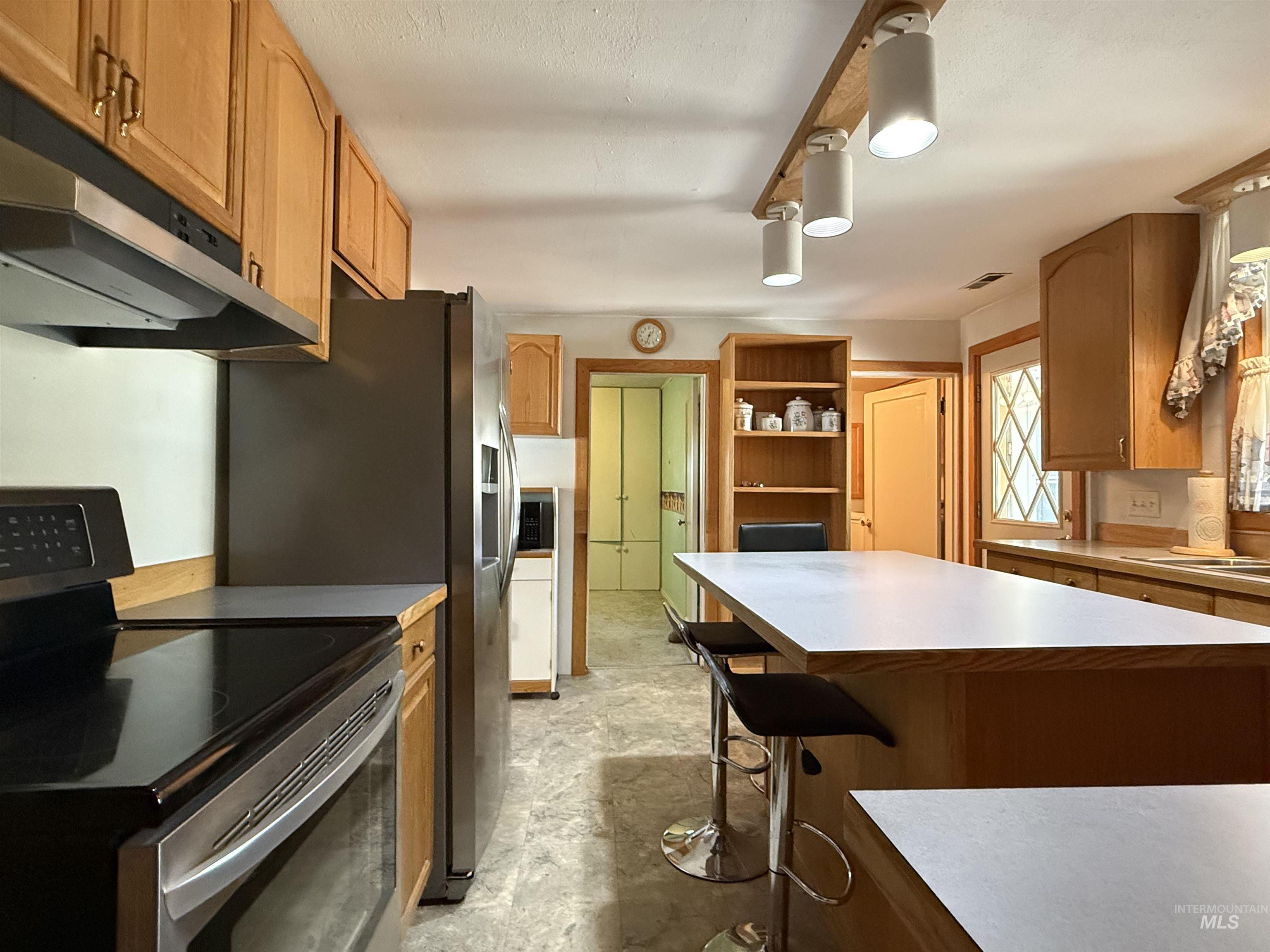 2395 Villard Street Pomeroy, WA 99347 - Photo 6 of 50 Kitchen with appliances with stainless steel finishes, light countertops, a breakfast bar, brown cabinets, and under cabinet range hood