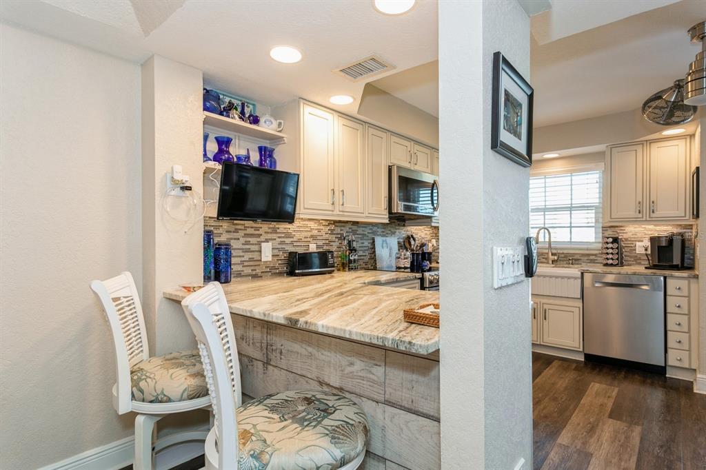 9166 Blind Pass Road St. Pete Beach, FL 33706 - Photo 12 of 37 a open kitchen with stainless steel appliances granite countertop a stove top oven a sink a dining table and chairs with wooden floor