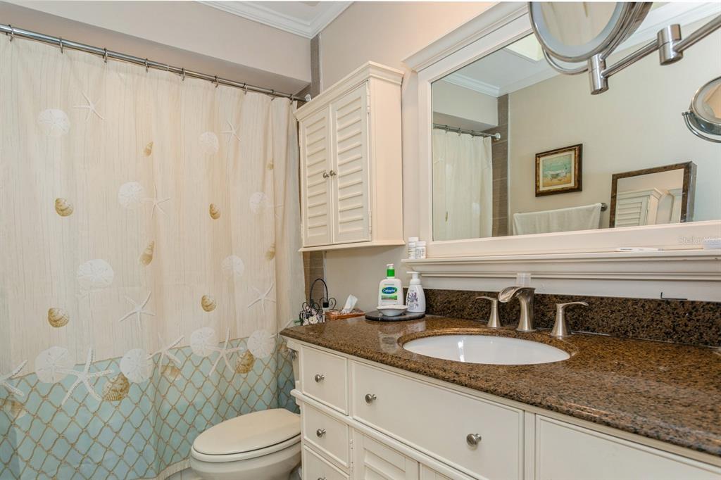 9166 Blind Pass Road St. Pete Beach, FL 33706 - Photo 19 of 37 a bathroom with a granite countertop sink a toilet a mirror and shower