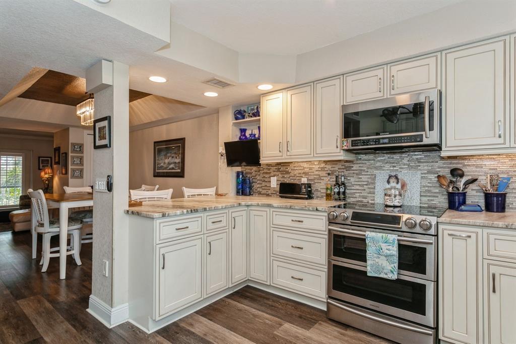 9166 Blind Pass Road St. Pete Beach, FL 33706 - Photo 8 of 37 a kitchen with stainless steel appliances granite countertop a stove top oven a sink dishwasher and white cabinets with wooden floor