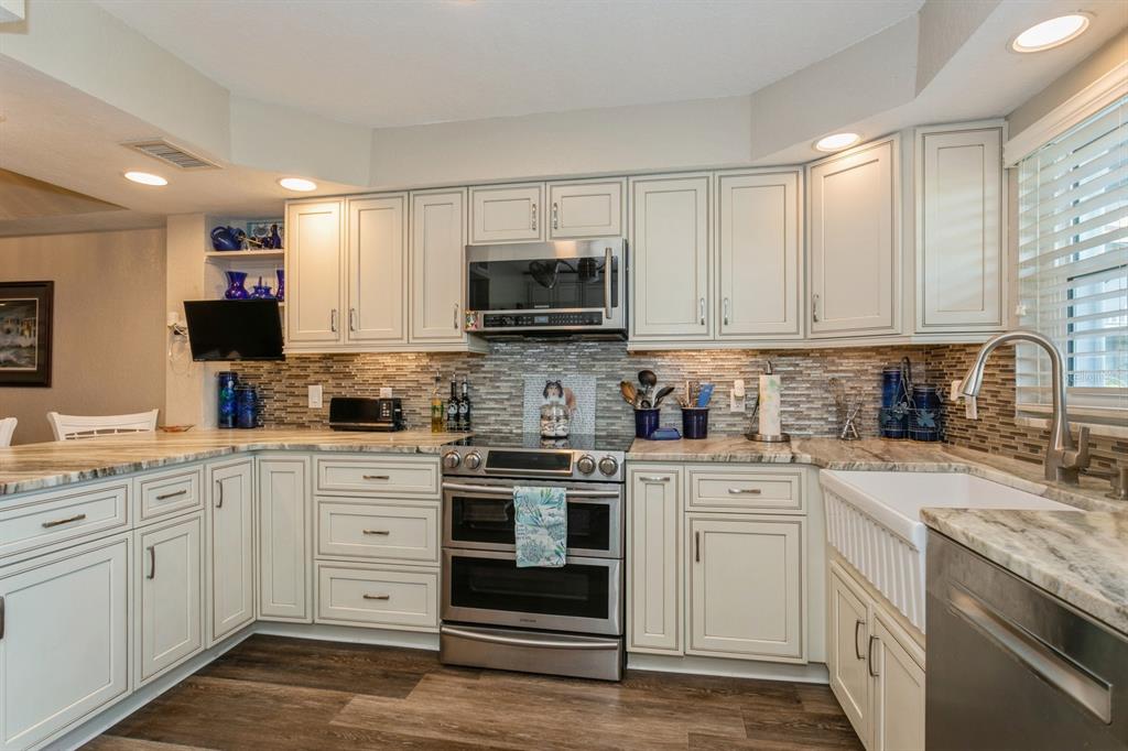 9166 Blind Pass Road St. Pete Beach, FL 33706 - Photo 9 of 37 a kitchen with stainless steel appliances granite countertop a stove top oven a sink dishwasher and a microwave oven with the cabinets