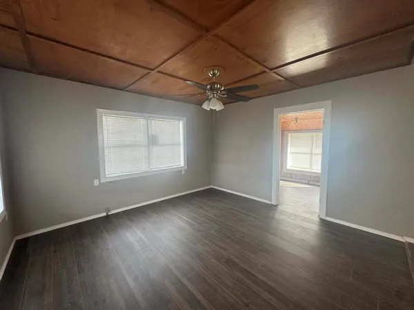 an empty room with wooden floor chandelier fan and windows