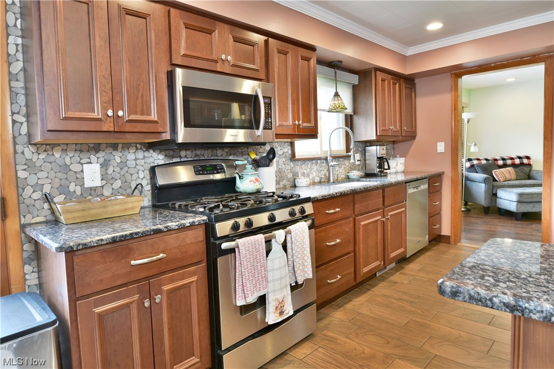 1711 Salt Springs Road Mineral Ridge, OH 44440 - Photo 13 of 35 Kitchen featuring backsplash, brown cabinets, ceramic flooring, crown molding, stainless steel appliances, and dark stone counters