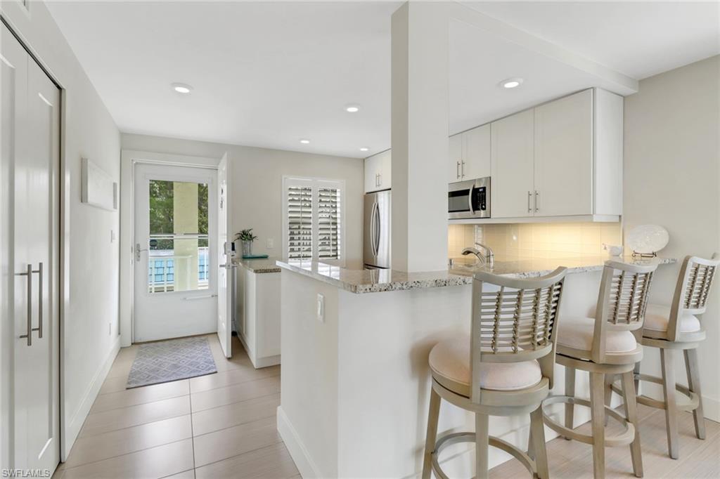 3055 Riviera Drive, Unit 201 Naples, FL 34103 - Photo 4 of 18 Kitchen featuring light stone counters, a breakfast bar, white cabinetry, decorative backsplash, and recessed lighting