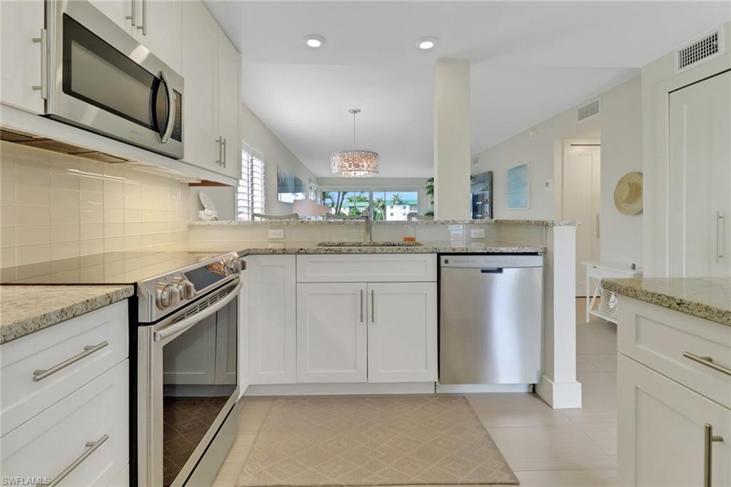 3055 Riviera Drive, Unit 201 Naples, FL 34103 - Photo 4 of 18 Kitchen with appliances with stainless steel finishes, white cabinets, pendant lighting, light stone counters, and decorative backsplash
