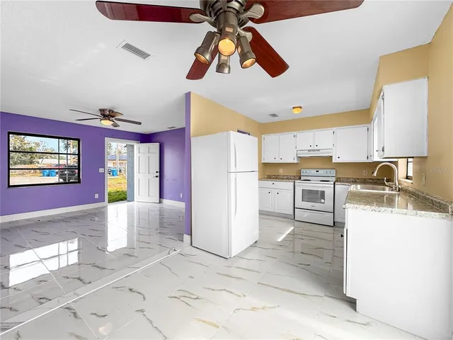 a large kitchen with granite countertop a refrigerator a sink a stove and white cabinets