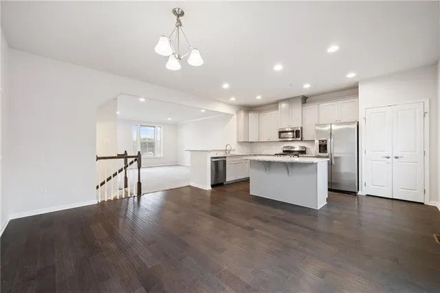 a living room with stainless steel appliances kitchen island granite countertop a stove a sink a refrigerator and white cabinets with wooden floor