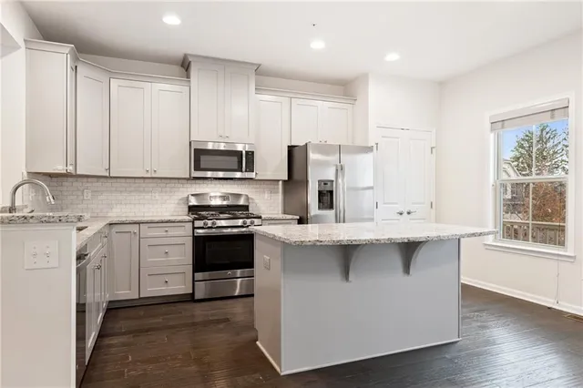 a kitchen with stainless steel appliances granite countertop a stove top oven a sink a refrigerator and white cabinets