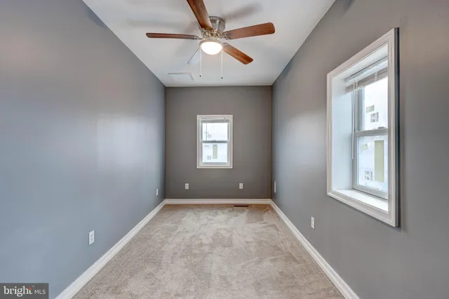 an empty room with chandelier fan and windows