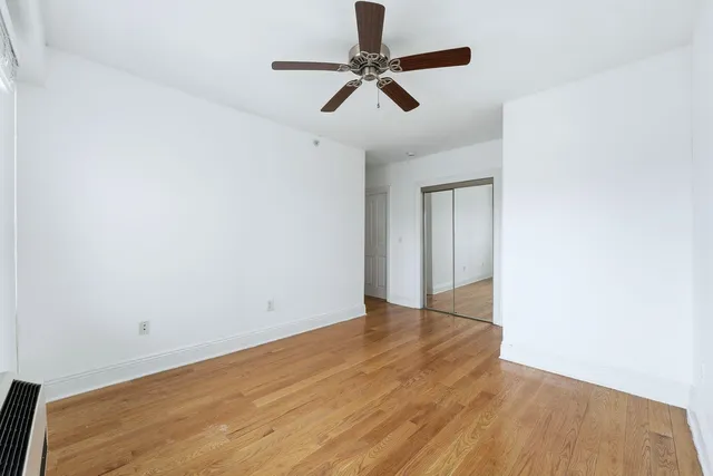 an empty room with wooden floor ceiling fan and window